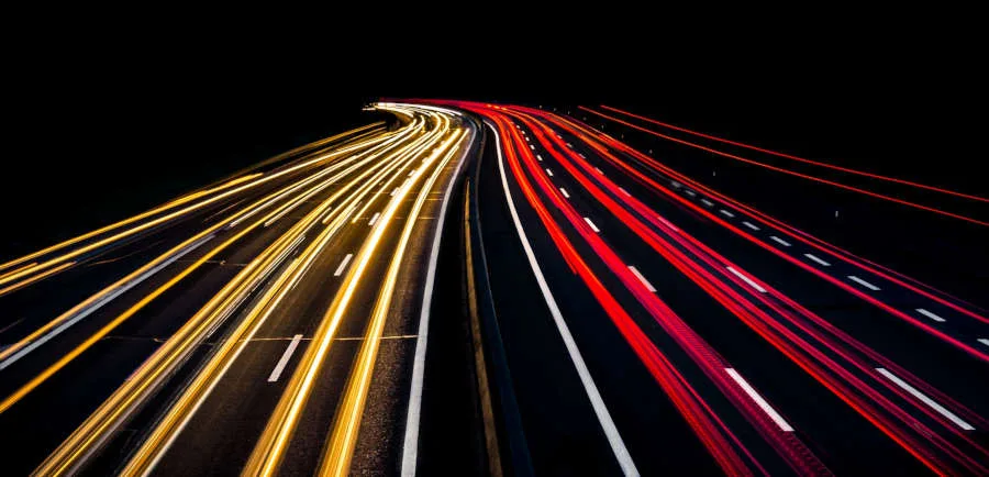 Time-lapse photo of road at night showing lights of speeding cars